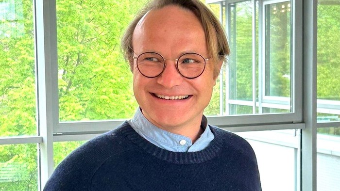 Ein Mann mit Brille und blauem Pullover lehnt auf einem Geländer