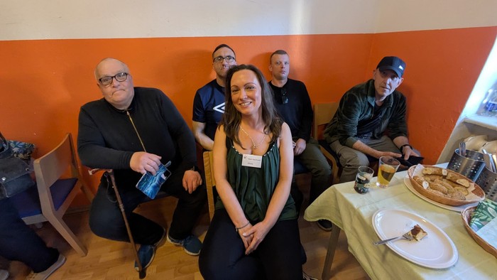 Einige Menschen schauen lächelnd in die Kamera, ein Tisch mit Essen steht dabei.