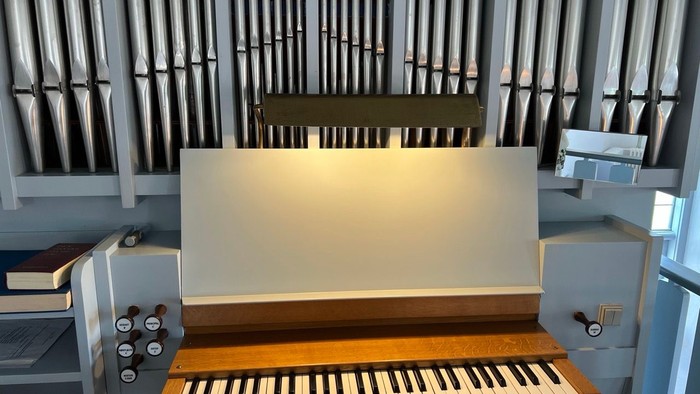Elegant pibeorgel med træklaver og rækker af polerede metalpiber bag en oplyst panel.