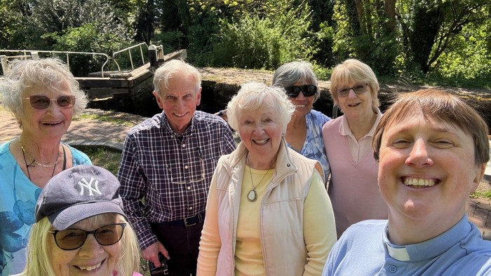 A cheerful group of seven people posing happily outdoors near a waterway.