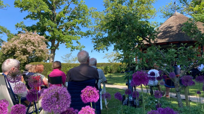 En gruppe mennesker sidder i træerne og ser ud over en blomstereng med lilla kogleblomster.