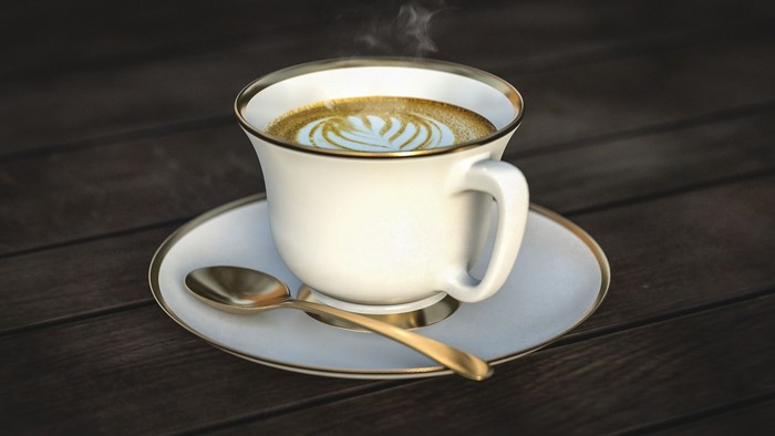 En dampende kop kaffe med latte kunst på en underkop, ledsaget af en ske på en træoverflade.