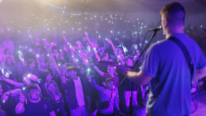 Begeisterte Menge jubelt und hält Handys hoch auf einem lebhaften Konzert unter violettem Licht.