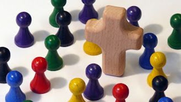 Bunte Plastikfiguren, die um einen hölzernen kreuzförmigen Block angeordnet sind.