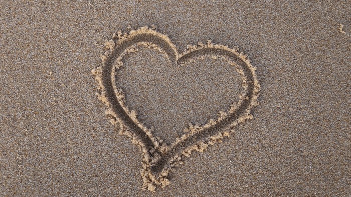 Ein Herz aus Sand am Strand gezeichnet.