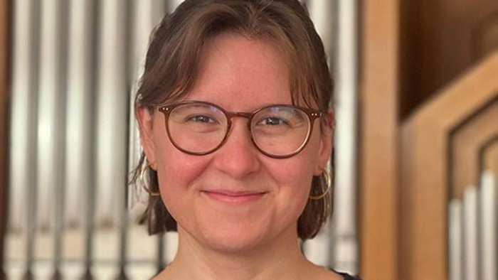 Eine Person mit Brille steht lächelnd vor einer großen Pfeifenorgel.