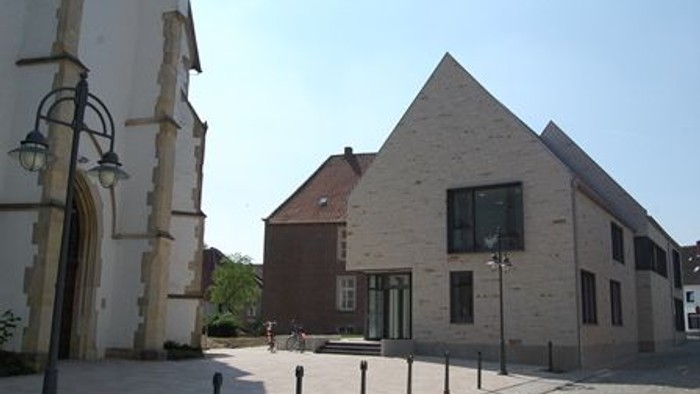 Das Bild zeigt eine Kirche und ein modernes Gebäude mit spitzem Dach.