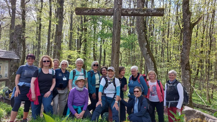 Gruppe von Wanderern, die gemeinsam in einem Wald in der Nähe eines großen Holzkreuzes posieren.