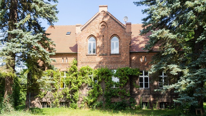 Ein charmantes Backsteinhaus, umgeben von üppigem Grün und hohen immergrünen Bäumen.