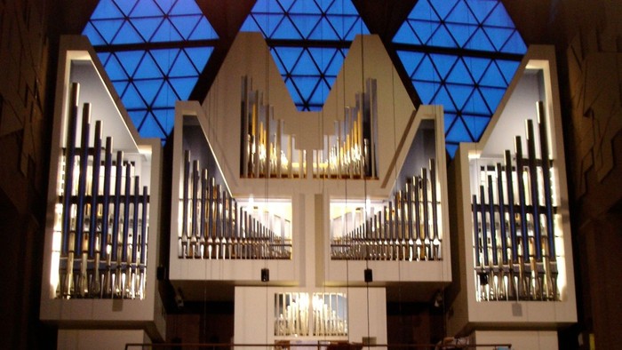 Große Pfeifenorgel in einer Kirche mit einer versammelten Gemeinde darunter während eines Abendgottesdienstes.