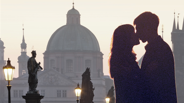 Paar in Silhouette, das einen romantischen Moment vor einer historischen Brücke und prächtigen Kuppelbauten bei Sonnenuntergang teilt.