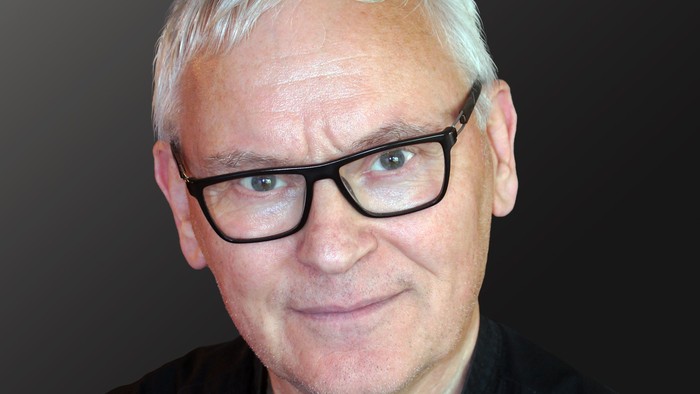 Günther Dreisbach, Prädikant in der evangelischen Kirchengemeinde Wolfhagen, schaut freundlich in die Kamera. Hintergrund ist dunkel.