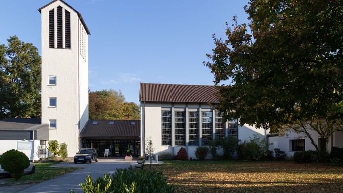 Moderne Kirchenanlage mit hohem Glockenturm, umgeben von gestalteten Grünflächen und Bäumen.