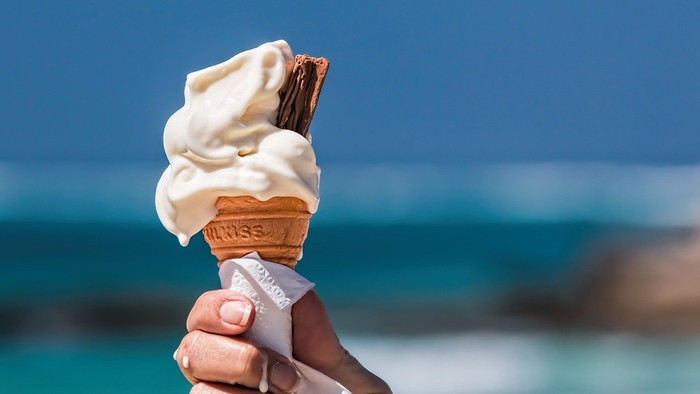 En hånd holder en iscreme med chokolade i en krumkake ved stranden