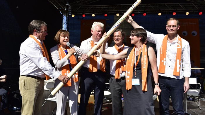 Eine Gruppe von Musikern feiert auf der Bühne mit Instrumenten und orangefarbenen Schals