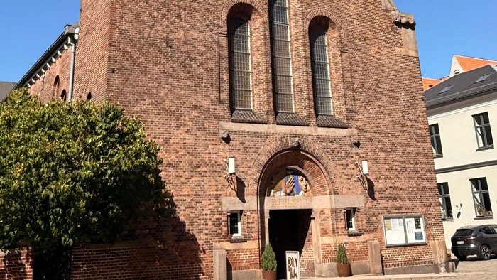 En historisk murstenskirke med højt klokketårn og buet indgang under klar blå himmel.