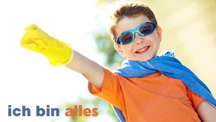 Ein fröhliches Kind in einem Superheldenumhang und Sonnenbrille spannt mit einem gelben Handschuh die Muskeln an und lächelt strahlend.