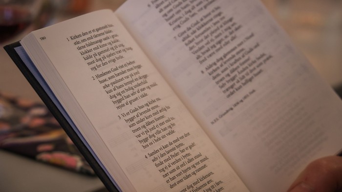 En åben bog med tekst, der bliver læst, sandsynligvis en religiøs eller historisk tekst, holdt af en hånd.