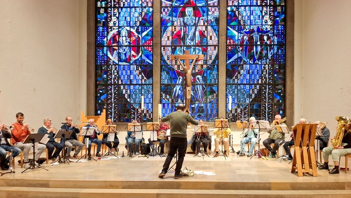 Ein Posaunenchor spielt in einer Kirche vor einem großen Kirchenfenster