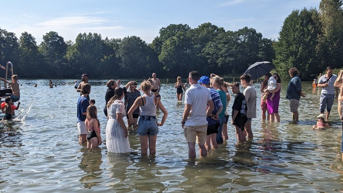 Eine Gruppe von Menschen steht im flachen Wasser eines Sees, einige halten Regenschirme.