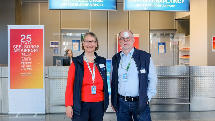 Zwei Flughafen-Seelsorger posieren für ein Foto am Flughafen Düsseldorf anlässlich des 25-jährigen Jubiläums des Seelsorgedienstes.