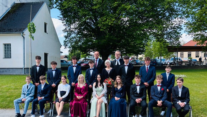 Absolventenklasse und Lehrkräfte posieren in formeller Kleidung vor einem kirchenähnlichen Gebäude.
