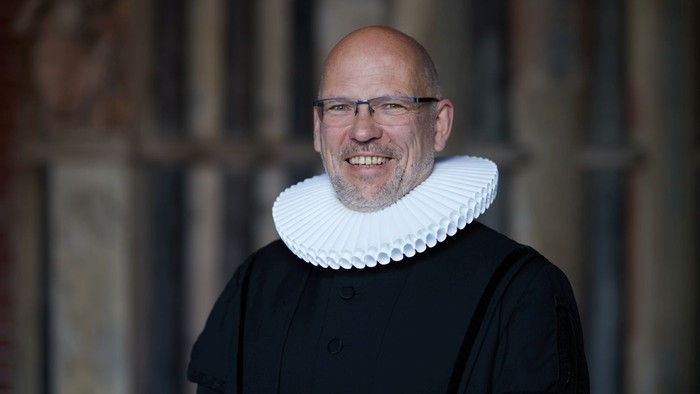 Mann in historical Kleidung mit Kragen und Brille lächelt