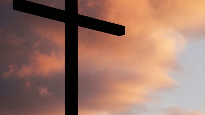 Ein Kreuz vor einem orangefarbenen Himmel bei Sonnenuntergang