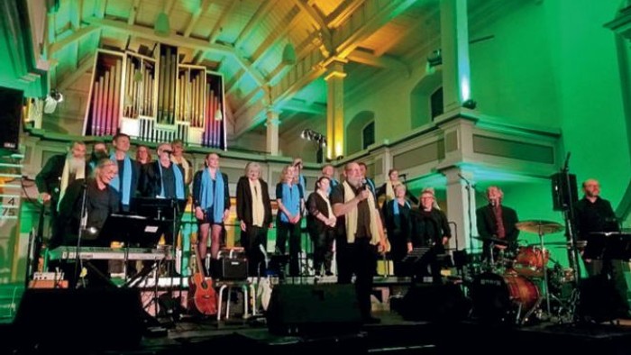 Der Gospel-Chor Zossen bei einem Auftritt zur Nacht der offenen Kirchen in der Kirche, die in grünen und gelben Farben ausgeleuchtet ist.