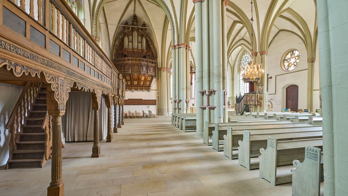 Historisches Kircheninneres mit verzierten Kirchenbänken, hohen Gewölbedecken und einer prächtigen hölzernen Kanzel.