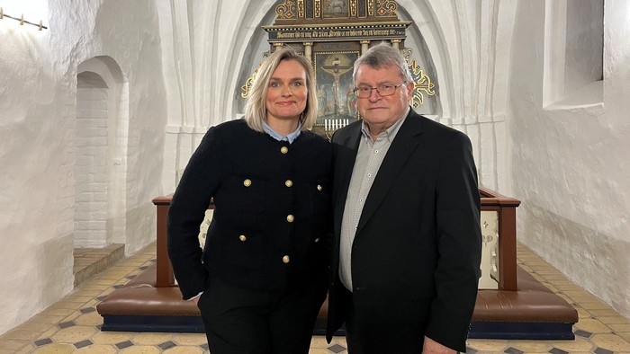 To personer poser formelt inde i et prægtigt, historisk kirkeinteriør med hvælvede lofter og kirkebænke.