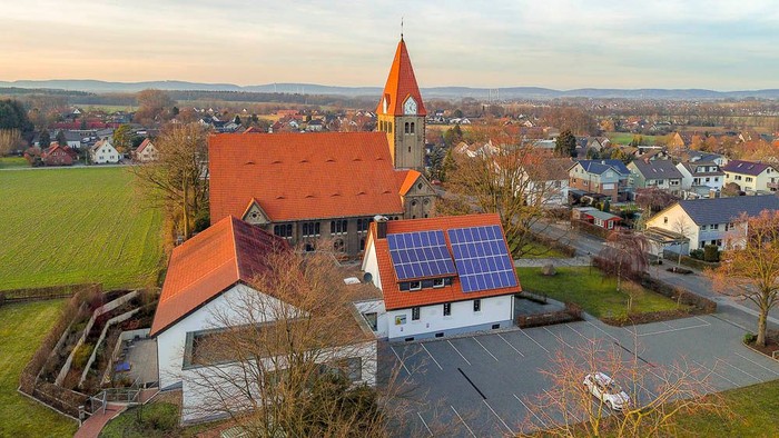 Luftaufnahme eines malerischen Dorfes mit einer Kirche mit Solarpaneelen und idyllischer Landschaft.