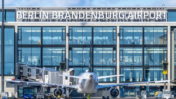 Flugzeug am Flughafen Berlin Brandenburg geparkt, mit angeschlossenem Boardingsteg, moderner Terminal im Hintergrund.