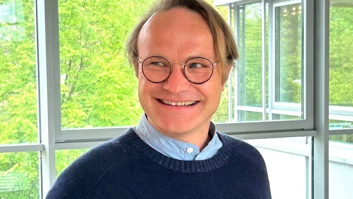 Ein Mann mit Brille und blauem Pullover lehnt auf einem Geländer