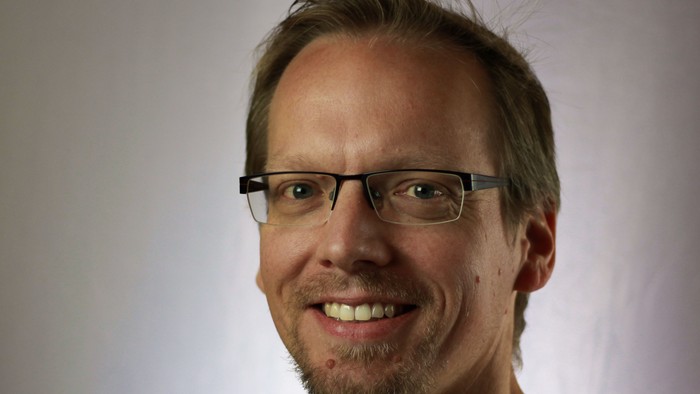 Portraitfoto von Pfarrer Christian Hoenemann, der lächelnd in die Kamera schaut. Er trägt eine Brille und einen gestreiften Pullover.