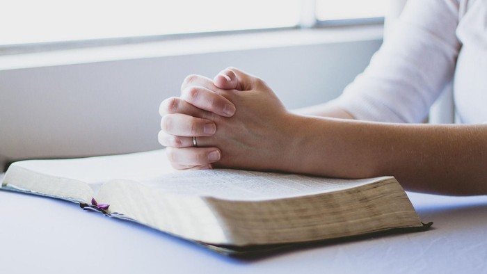 Eine Person im Gebet mit gefalteten Händen über einem geöffneten Buch, wahrscheinlich einer Bibel.
