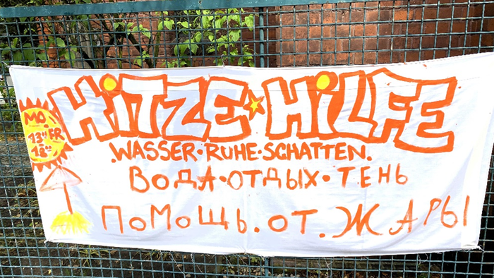 Handbemaltes Banner in mehreren Sprachen mit dem Aufruf, bei Hitze mit Wasser, Ruhe und Schatten zu helfen.
