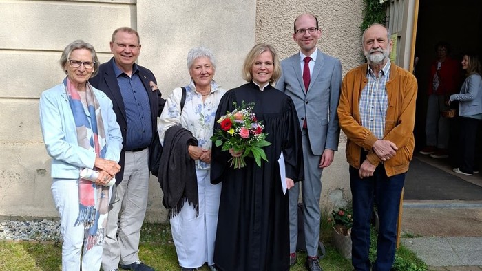 Gruppe von sieben Personen, die vor einem Gebäude posieren, wobei eine Person einen Blumenstrauß hält.