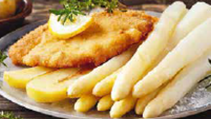 Goldener frittierter Fisch serviert mit cremigem Kartoffelpüree und gedünsteten Spargelspitzen, garniert mit Kräutern.