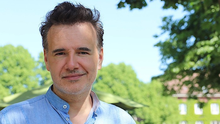 Christian Martin Lukas lächelt in die Kamera, im Hintergrund sind frühlingsgrüne Bäume zu sehen.