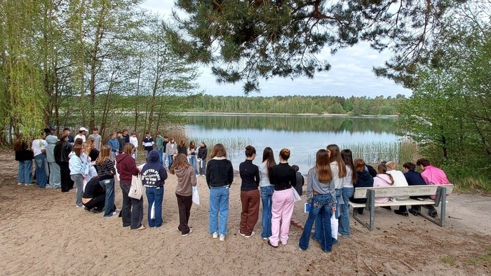 Jugendliche aus der Konfi-Gruppe stehen und sitzen gemeinsam am Ufer eines Sees, umgeben von Bäumen und Wasser. Die ruhige Atmosphäre und die Gemeinschaft unter freiem Himmel spiegeln die Themen von Pfingsten, Zusammenhalt und gemeinsamem Glauben wider.