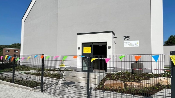 Großes graues Gebäude mit einem Zaun vorne dran, an dem eine bunte Girlande hängt