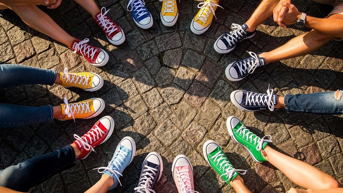 Eine vielfältige Gruppe bunter Sneaker, die im Kreis auf einem Kopfsteinpflaster angeordnet sind.