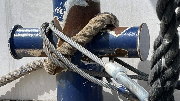 Verwitterte blaue Festmacherpoller, die mit dicken Tauen an einem Kai oder Schiffsdeck befestigt sind.