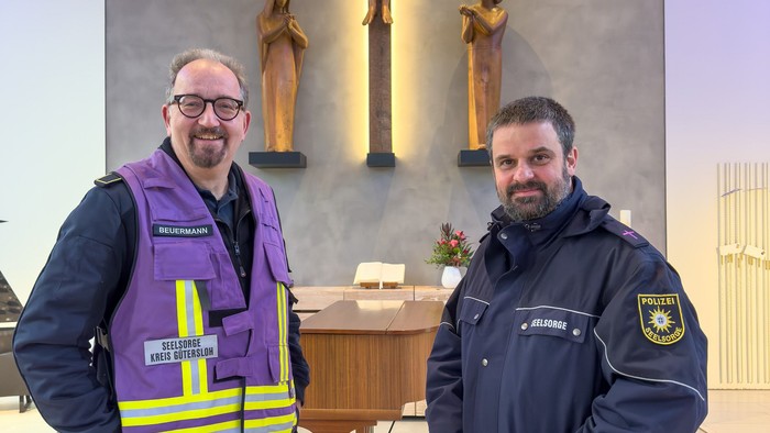 Zwei Männer in Uniformen stehen in einer Kirche in der Nähe eines Kruzifixes und eines Altars.