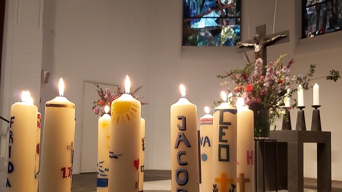 Kirchliche Kerzen mit Namen und Herzen, davor ein Blumenstrauß