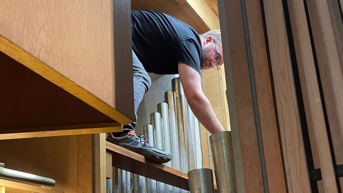 Eine Person steigt eine Leiter hinauf, um die Pfeifen einer großen Orgel zu erreichen und einzustellen.