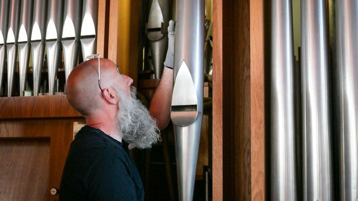 Ein Mann mit langem Bart entfernt eine große Pfeife aus einer Orgel