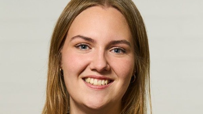 En glad ung kvinde med glat blondt hår iført en grøn sweater og smilende til kameraet.
