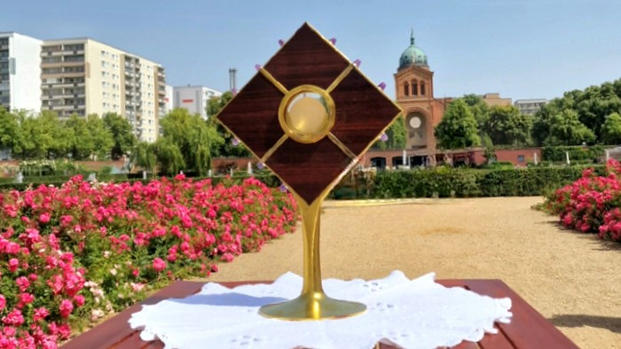 Ein Tisch mit einem goldenen Objekt und Kerzen im Garten, im Hintergrund Gebäude und Blumenbeete